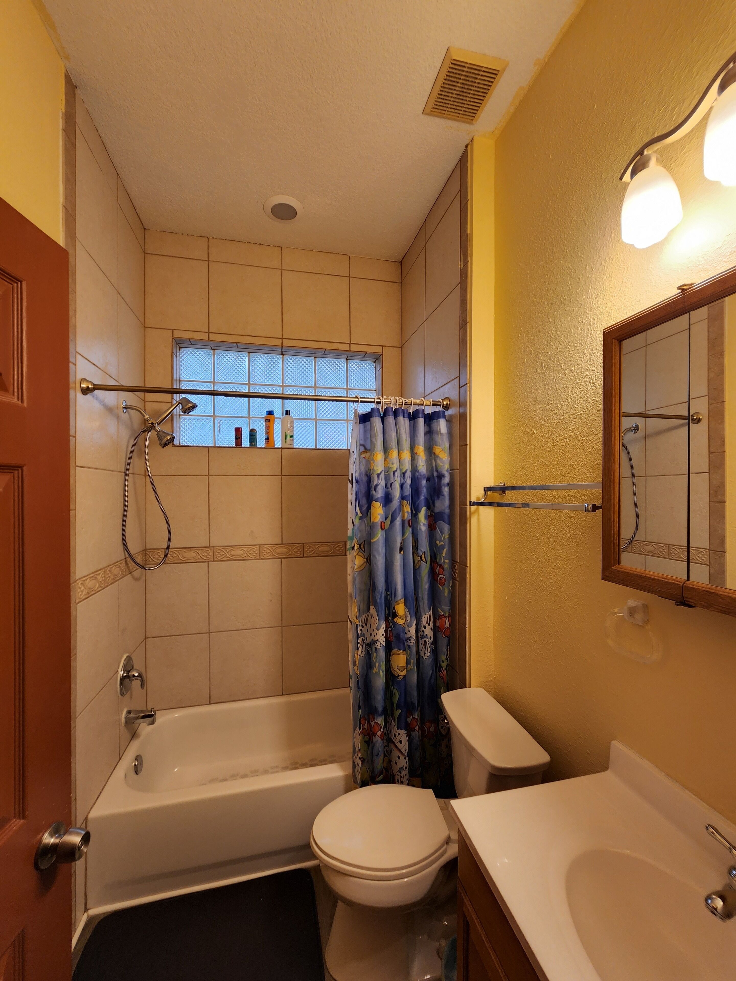 A bathroom with a bathtub, toilet, and sink. There is a window with a view of the outside, a shower curtain, and a towel rack.