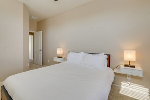 A bedroom with a large bed, two bedside tables with lamps, and a door leading to another room. - Pool, Fire Pit: Luxe Family Home in Goodyear (Goodyear)