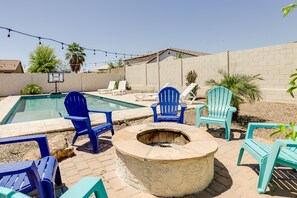 A backyard with a swimming pool, blue Adirondack chairs, a fire pit, and a basketball hoop. - Pool, Fire Pit: Luxe Family Home in Goodyear (Goodyear)