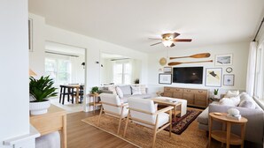 A spacious living room with a wooden floor, a ceiling fan, a TV, and a sofa. - New! Refreshed modern coastal retreat in Duck! (Kitty Hawk)