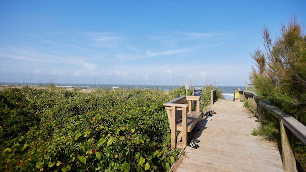 A wooden boardwalk leading to a beach with a bench and a sign. - New! Refreshed modern coastal retreat in Duck! (Kitty Hawk)