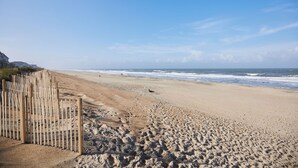 A sandy beach with footprints leading to the water, a wooden fence, and a clear sky. - New! Refreshed modern coastal retreat in Duck! (Kitty Hawk)