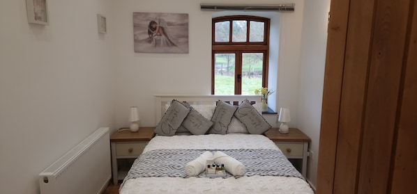 A neatly made bed with patterned bedding, a window with a view of greenery, and a wall-mounted picture.