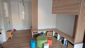 Een kamer met een stapelbed, een klein bureau, een stoel en een opbergkast met speelgoed en boeken.