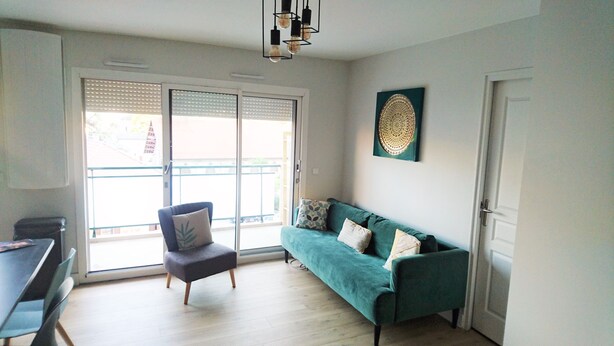 Een moderne woonkamer met een blauwgroene bank, een fauteuil en een eettafel.