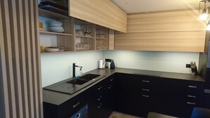 Een moderne keuken met zwarte kastjes, een roestvrijstalen spoelbak en houten planken met borden en glazen.