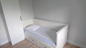 Een kleine, witte kamer met een enkel bed, een houten vloer, een witte kast en een witte radiator.