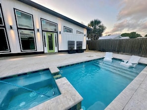 A modern house with a swimming pool, a green door, and a wooden fence.