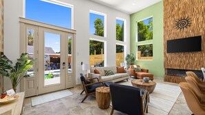 A spacious living room with large windows, a fireplace, and a flat-screen TV mounted on a wooden wall. - 2 Homes 1 Incredible Stay*Private Pool & 5 Kings! (Panama City Beach)