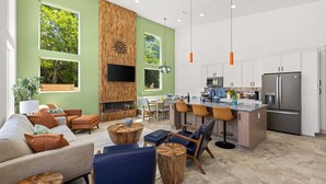 A modern living room with a fireplace, a kitchen with stainless steel appliances, and large windows. - 2 Homes 1 Incredible Stay*Private Pool & 5 Kings! (Panama City Beach)