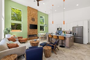 A modern living room with a fireplace, a kitchen with stainless steel appliances, and large windows. - 2 Homes 1 Incredible Stay*Private Pool & 5 Kings! (Panama City Beach)
