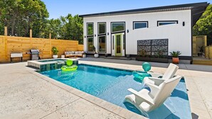 A modern house with a swimming pool, outdoor seating, and a wooden fence.