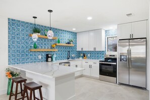 Eine moderne Küche mit weißen Schränken, einer Marmorarbeitsplatte und einer blau gemusterten Spritzschutzwand.