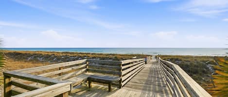 A wooden boardwalk leading to a beach with benches.
