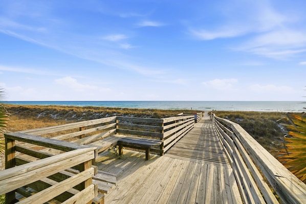 A wooden boardwalk leading to a beach with benches.