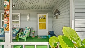 A porch with a wooden bench, a chair, and a door with a yellow window.