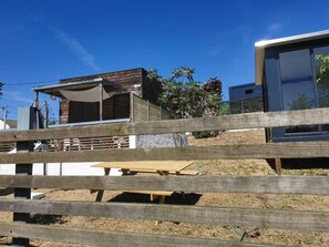 A wooden fence, a picnic table, and a building with a wooden facade and a white awning. - tiny house in the nature , near of beautiful beaches (Setubal)
