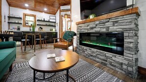 A modern living room with a stone fireplace, a television mounted above it, and a dining area with chairs and a table.