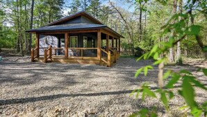 A wooden cabin with a covered porch, surrounded by trees.