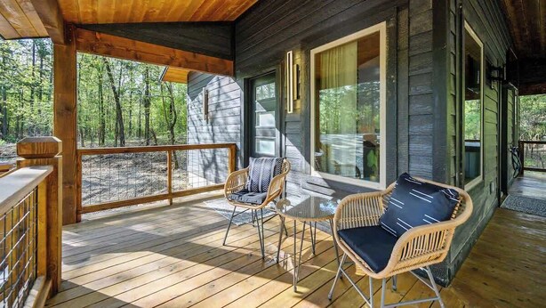 A wooden deck with wicker furniture, large windows, and a view of the forest.