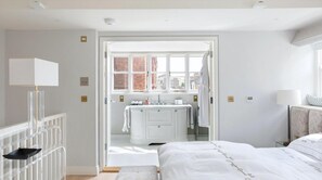 Relax in a serene bedroom with a large bed, bedside table, and en-suite bathroom featuring a bathtub and city view.