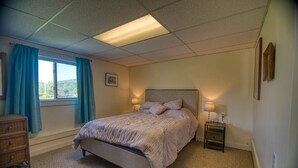 A bedroom with a bed, two bedside tables with lamps, a dresser, a window with curtains, and a picture on the wall. - Cozy renovated barn apartment on first floor (Randolph Center)
