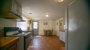 A kitchen with a stove, cabinets, and a dining table with chairs. - Cozy renovated barn apartment on first floor (Randolph Center)