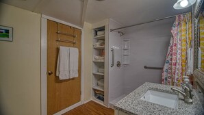 A compact bathroom with a shower, a sink with a granite countertop, and a wooden door with a towel hanging. - Cozy renovated barn apartment on first floor (Randolph Center)
