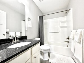 Bathroom features a granite countertop sink, a white toilet, a separate bathtub, and a shower curtain.