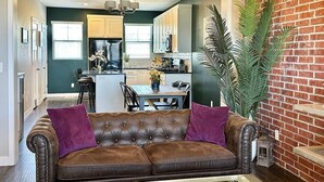 A modern kitchen with white cabinets, a dining area with a wooden table and chairs, and a leather sofa with purple cushions. - Charming updated LOFT style townhouse!!! (Midvale)