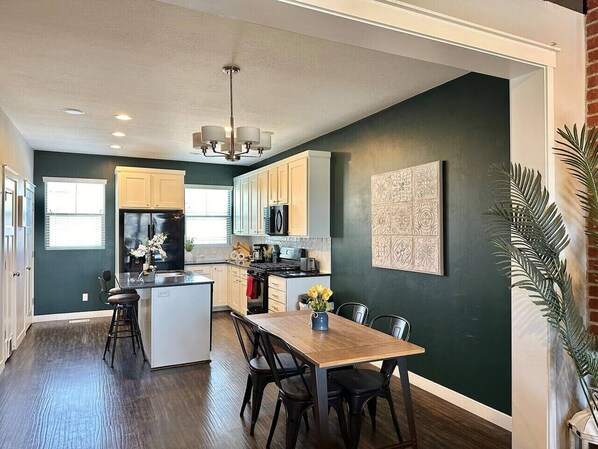 A kitchen with a central island, wooden flooring, and a dining area with chairs and a table.