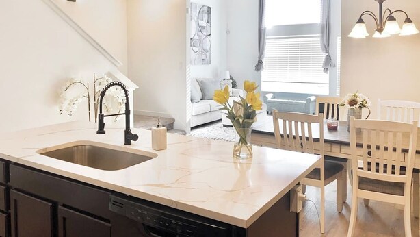 A modern kitchen with a large island, a built-in dishwasher, and a dining area with a table and chairs.