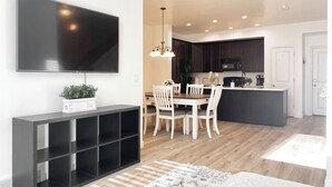 A modern kitchen with dark cabinets, a central island, and a dining area with white chairs.