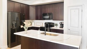 A modern kitchen with dark wood cabinets, a stainless steel refrigerator, a black microwave, and a white marble countertop.