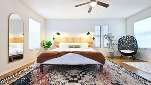 Quarto com cama, ventilador de teto, cadeira e uma janela grande.