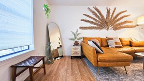 Uma sala de estar com um sofá de couro marrom, uma mesa de centro de vidro, um banco de madeira, uma mesinha de apoio com uma planta e um espelho grande.