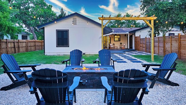 Um quintal com lareira, quatro cadeiras Adirondack e uma pérgola de madeira com luzes de cordão.