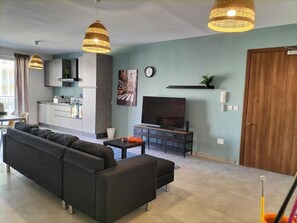 Een moderne woonkamer met een zwarte bank, een televisie en hanglampen.