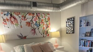 A bedroom with a bed, bedside tables, a bookshelf, and a decorative wall piece. - WorldCup Central- Easy access for sports and entertainment. (Houston)