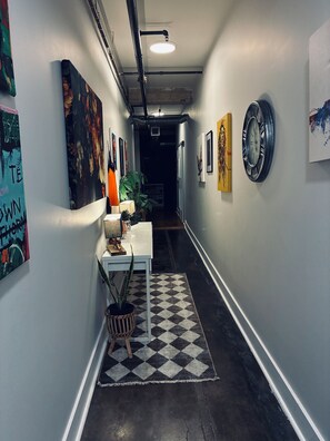 En gang med kunst på væggene, et bord med en lampe og et ternet tæppe på gulvet.