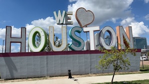 A large outdoor sign with the words "WE ♥ HOUSTON" in bold letters, set against a clear sky with clouds. - WorldCup Central- Easy access for sports and entertainment. (Houston)