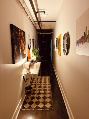 A hallway with artwork on the walls, a table with a plant, and a patterned rug. - WorldCup Central- Easy access for sports and entertainment. (Houston)
