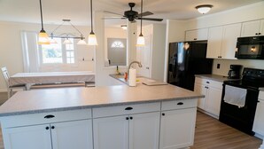 Une cuisine moderne avec des meubles blancs, un grand îlot central, un réfrigérateur noir et un ventilateur de plafond.