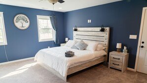 Une chambre à coucher avec un lit, des tables de chevet, un ventilateur de plafond et une fenêtre avec des rideaux.