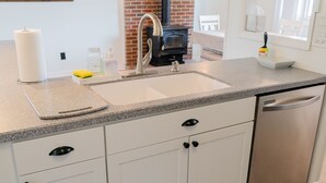 Une cuisine avec des armoires blanches, un comptoir en granit, un dosseret en briques, un lave-vaisselle en acier inoxydable et un tapis à motifs.