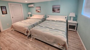 Une chambre avec deux lits, une porte, un appareil de climatisation et des œuvres d’art accrochées au mur.