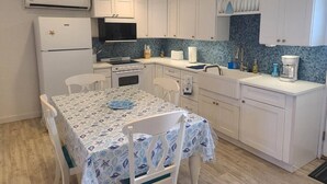 Une cuisine compacte avec des meubles blancs, une table à manger avec des chaises et un four encastré.