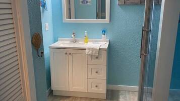 A bathroom with a sink, mirror, and shower area.