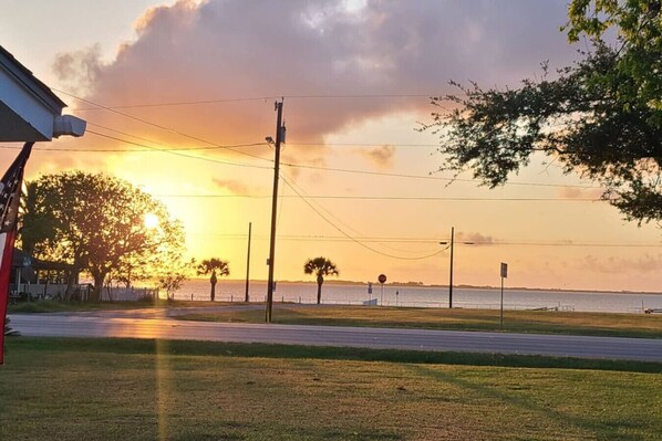 A sunset view with a road, trees, and a body of water.