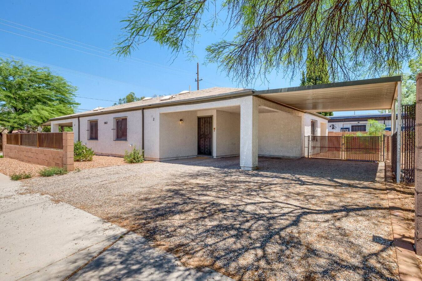 A single-story house with a covered porch, a gravel driveway, and a fenced yard.
